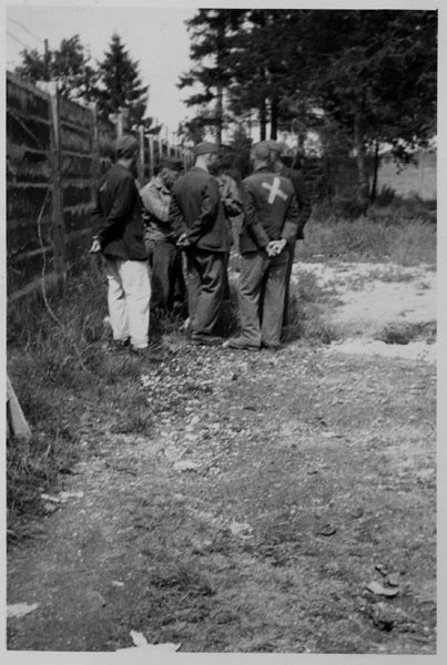 Inmates wearing their prison garb, looking at graves that they were forced to dig. The cross on the man's back marks a precise target for the Nazis to shoot at if the prisoner attempted to escape.
